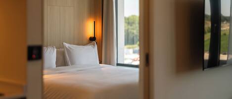 Habitación de hotel con una cama, televisor montado en la pared y ventana con vistas a zonas verdes.