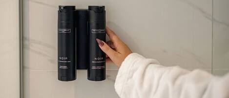 A hand holding two black bottles labeled "NOIR" on a marble wall.