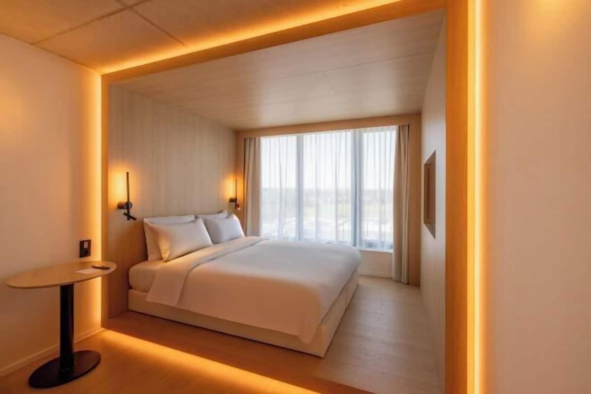 Una habitación de hotel con cama, mesita de noche, ventana con cortinas y una lámpara de pared.