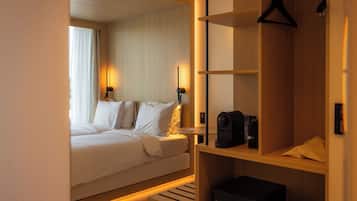 A hotel room with a bed, bedside lamps, a coffee machine, and a wooden wardrobe.