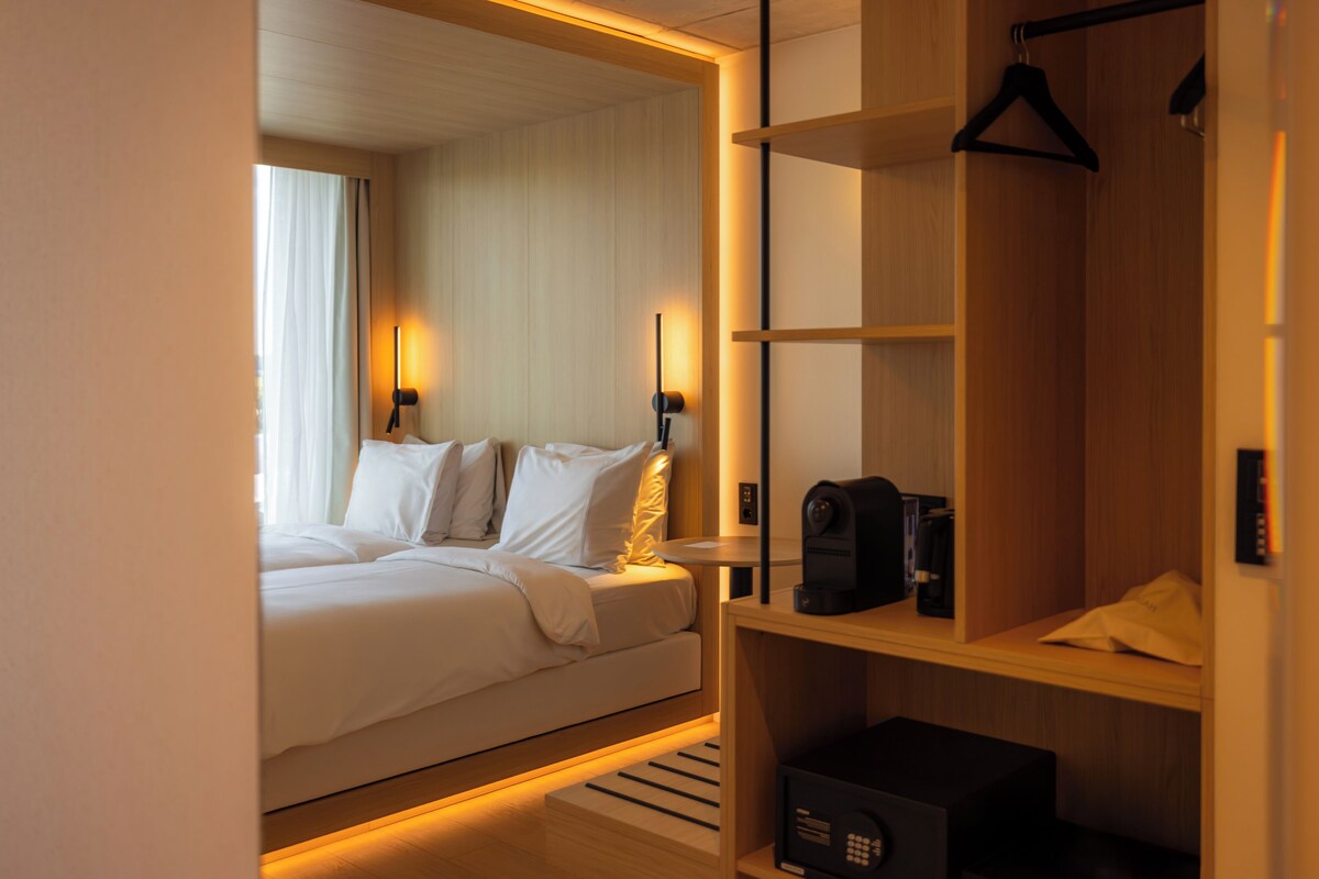 Une chambre d’hôtel avec un lit, des lampes de chevet, une machine à café et une armoire en bois.