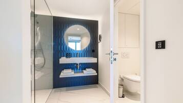 Un baño moderno con cabina de ducha de vidrio, un espejo redondo y un lavabo blanco con una pared de acento azul.