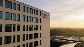 A modern hotel building with a flat facade, multiple windows, and a rooftop with solar panels. - NOTO Hotel (Reckange-sur-Mess)