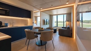 A modern kitchen with dark cabinets, a round dining table, and chairs. There is a large window with a view of the outdoors. - NOTO Hotel (Reckange-sur-Mess)