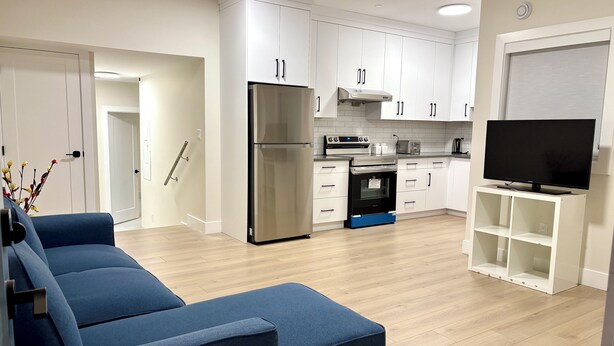 Una cocina moderna con armarios blancos, un refrigerador de acero inoxidable, horno empotrado y un televisor sobre un pedestal blanco.