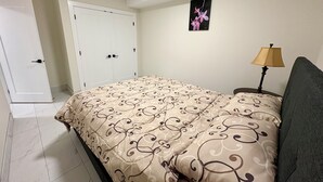 Un dormitorio con cama, mesita de noche, lámpara, puerta y un cuadro en la pared.