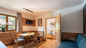 A cozy room with a wooden dining table, chairs, a blue sofa, and a view of the countryside through a large window. - Apartment in Brixental (Brixen im Thale)