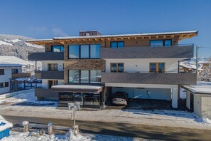 Une maison moderne à plusieurs étages, dotée d’un garage, de grandes fenêtres et offrant une vue sur des montagnes enneigées.