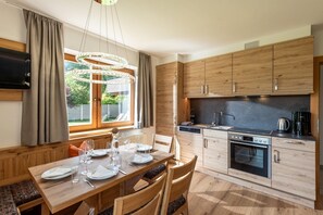 Une cuisine moderne avec des meubles en bois, un four encastré et un coin repas avec une table dressée pour quatre personnes.