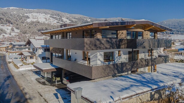 A modern multi-story building with large windows, a flat roof, and a ski slope in the background. - Apartment in Brixental (Brixen im Thale)