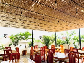 An outdoor dining area with bamboo ceiling, wooden tables, and chairs, surrounded by potted plants. - Crosswinds Residences (Paranaque)