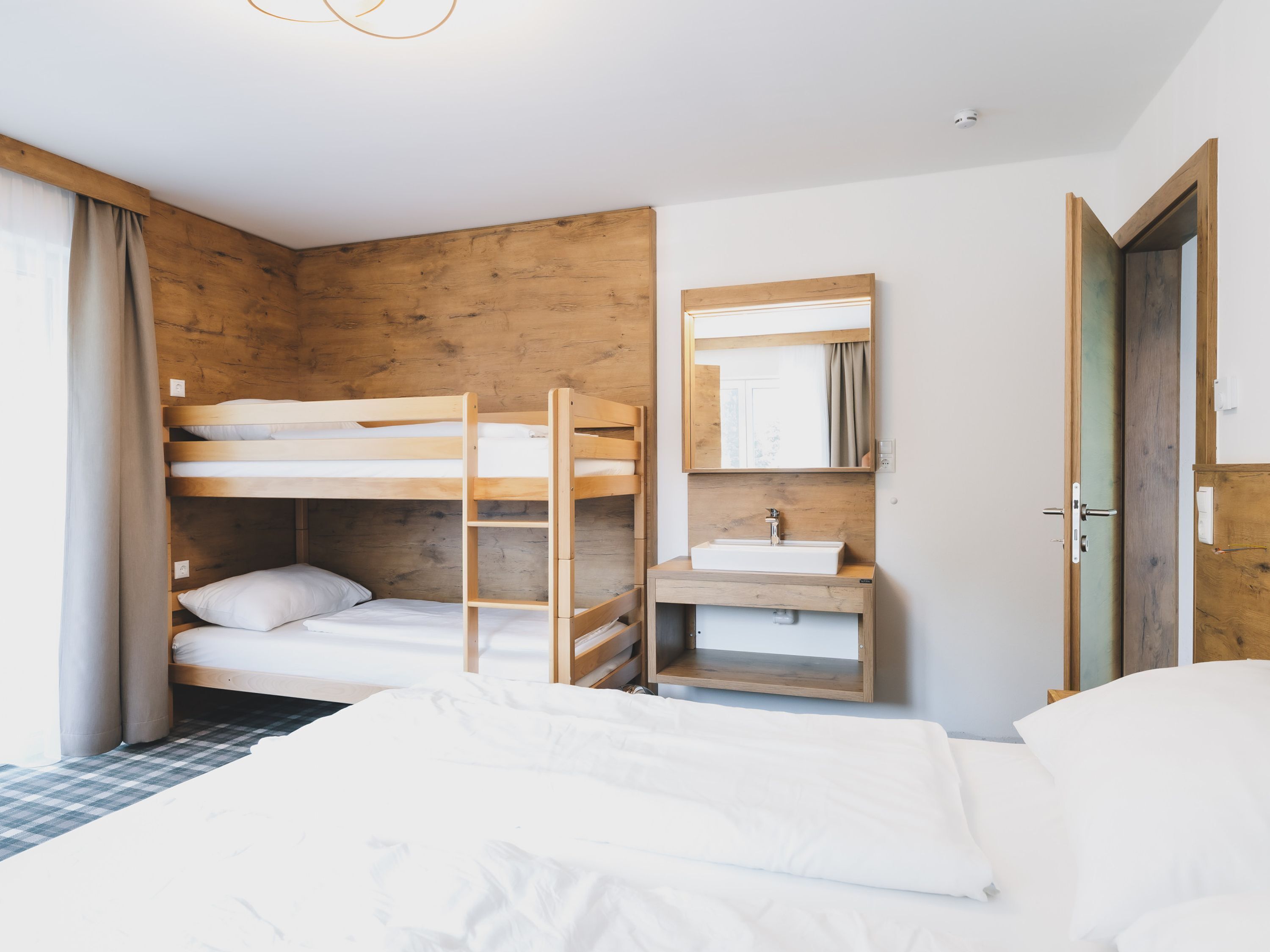 A bunk bed room with a wooden wall, a sink, and a mirror.