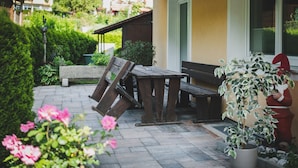 Eine Terrasse mit Holztisch und Bank, umgeben von Blumentöpfen und Blumen.