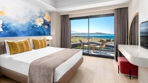 Ein Hotelzimmer mit einem großen Bett, einem Schreibtisch, einem Fernseher und einem Balkon mit Meerblick.