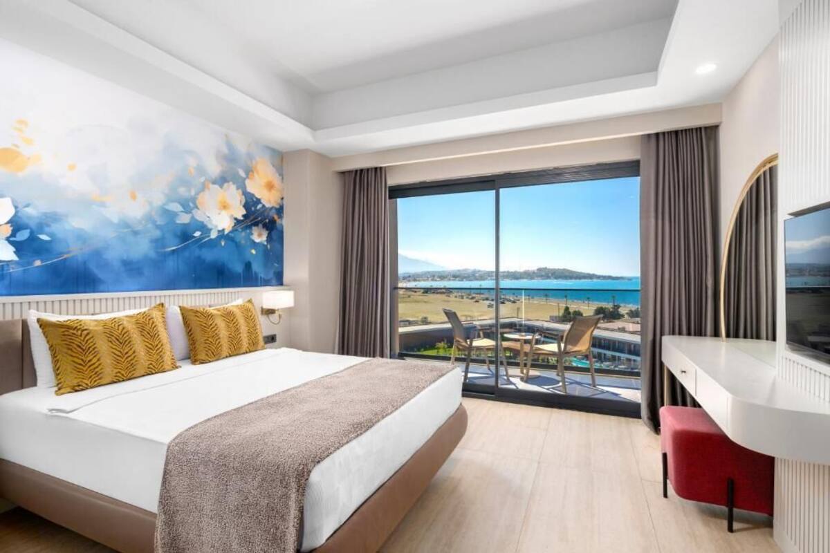 Een hotelkamer met een groot bed, een bureau, een televisie en een balkon met uitzicht op zee.