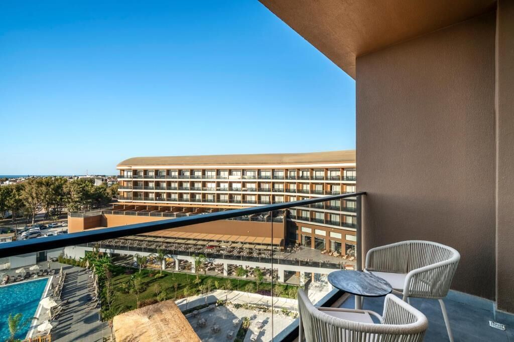 Un balcó amb una piscina, dues cadires de vimet i vista d'un gran edifici d'hotel.