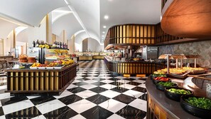Ein Buffetbereich mit Schachbrettmuster-Boden, unterschiedlichen Speiseausgaben und einer Bar mit Kupferdecke.