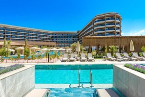 Ein Hotel mit Schwimmbad, Liegestühlen und einem großen Gebäude mit mehreren Balkonen.
