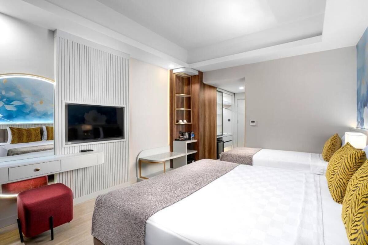 Een hotelkamer met een televisie, twee bedden, een bureau en een rode poef.