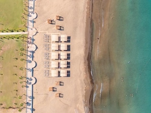Vista aérea de um hotel à beira-mar, com fileiras de quartos, uma praia arenosa e um oceano azul cristalino.