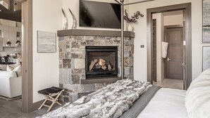 Un dormitorio con chimenea de piedra, una cama, un televisor sobre la chimenea y una puerta a la derecha.