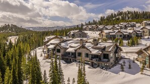 Un complejo turístico cubierto de nieve con varias construcciones de estilo chalet, rodeado de bosques frondosos y un camino sinuoso.