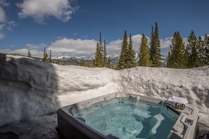 Un jacuzzi con vistas despejadas a montañas nevadas y árboles de hoja perenne al fondo.