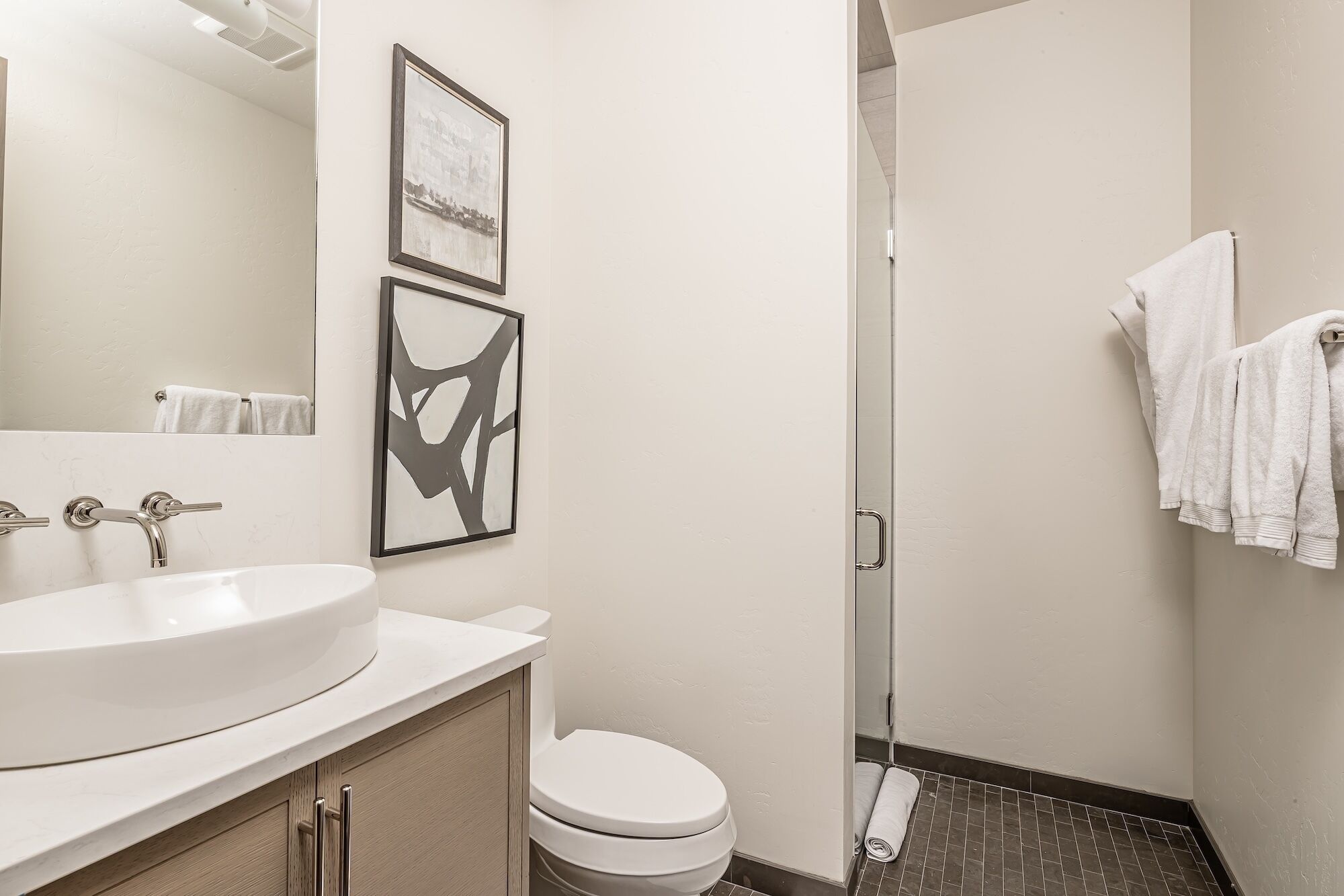 A bathroom with a white sink, a toilet, and a shower. There are two framed pictures on the wall.