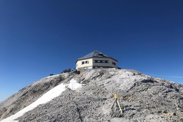 A mountain lodge with a conical roof, located on a rocky hill with a clear sky.