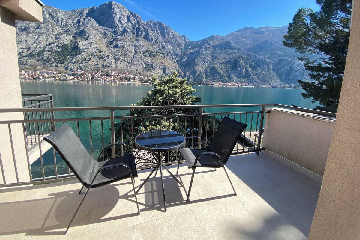 A balcony with a table and chairs overlooking a lake and mountains.