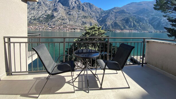 Un balcon avec une table et des chaises, donnant sur un lac et des montagnes.