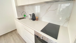 Une cuisine moderne avec des meubles blancs, un dosseret en marbre, un four encastré et une plaque de cuisson à induction noire.