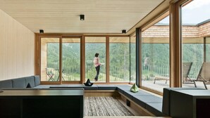 A modern interior with large windows, a wooden ceiling, and a seating area with a view of the outdoors. - Chalet Resort near Lake (Kals am Großglockner)