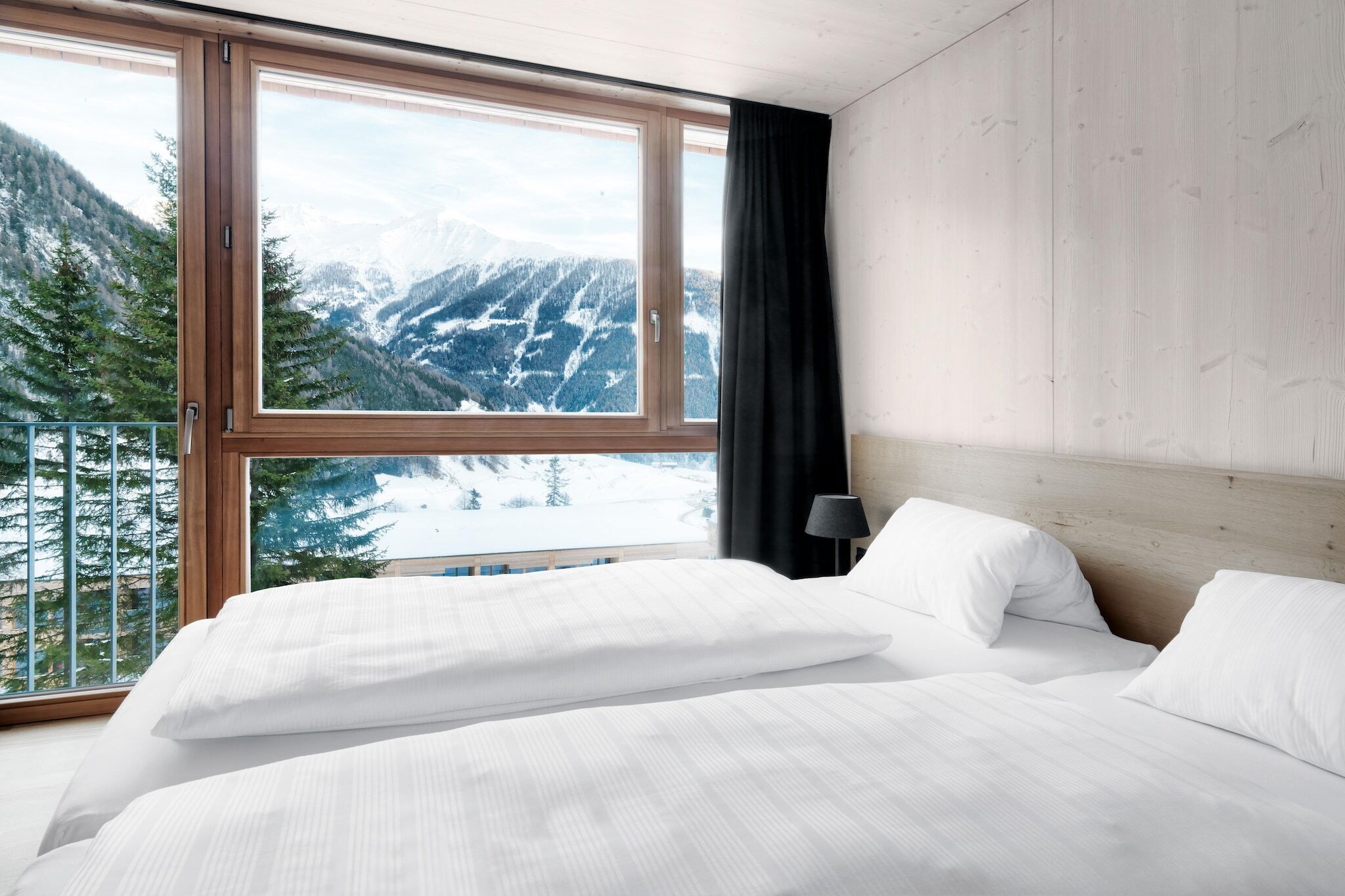 Ein Schlafzimmer mit großem Fenster und Bergblick, einem Holzkopfende und weißer Bettwäsche.