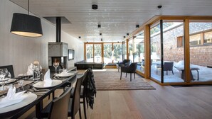 A modern dining area with a long table set for a meal, a fireplace, and a view of a snowy outdoor area through large glass doors. - Chalet Resort near Lake (Kals am Großglockner)
