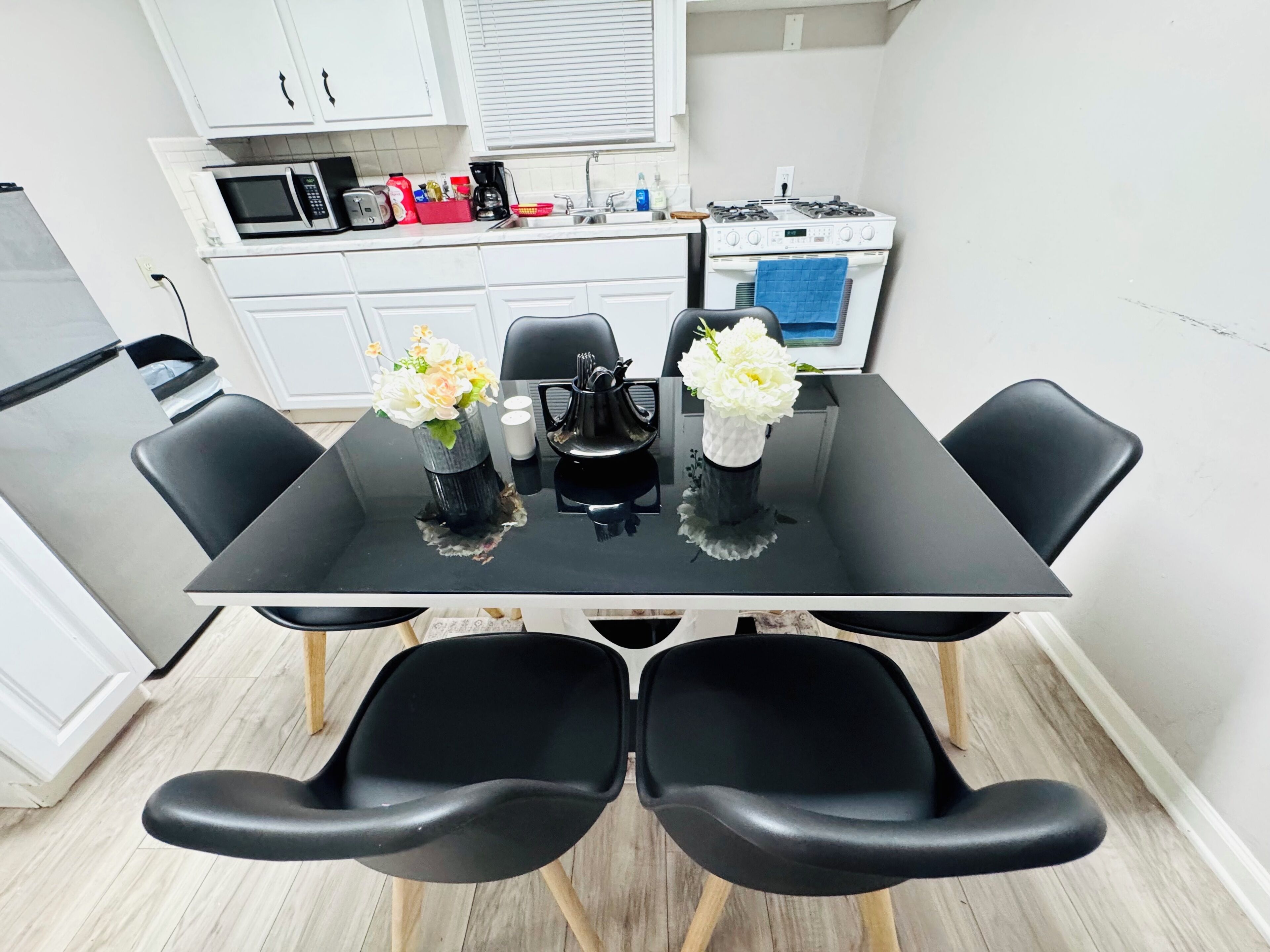 A modern kitchen with white cabinets, a microwave, a stove, and a dining table with black chairs.