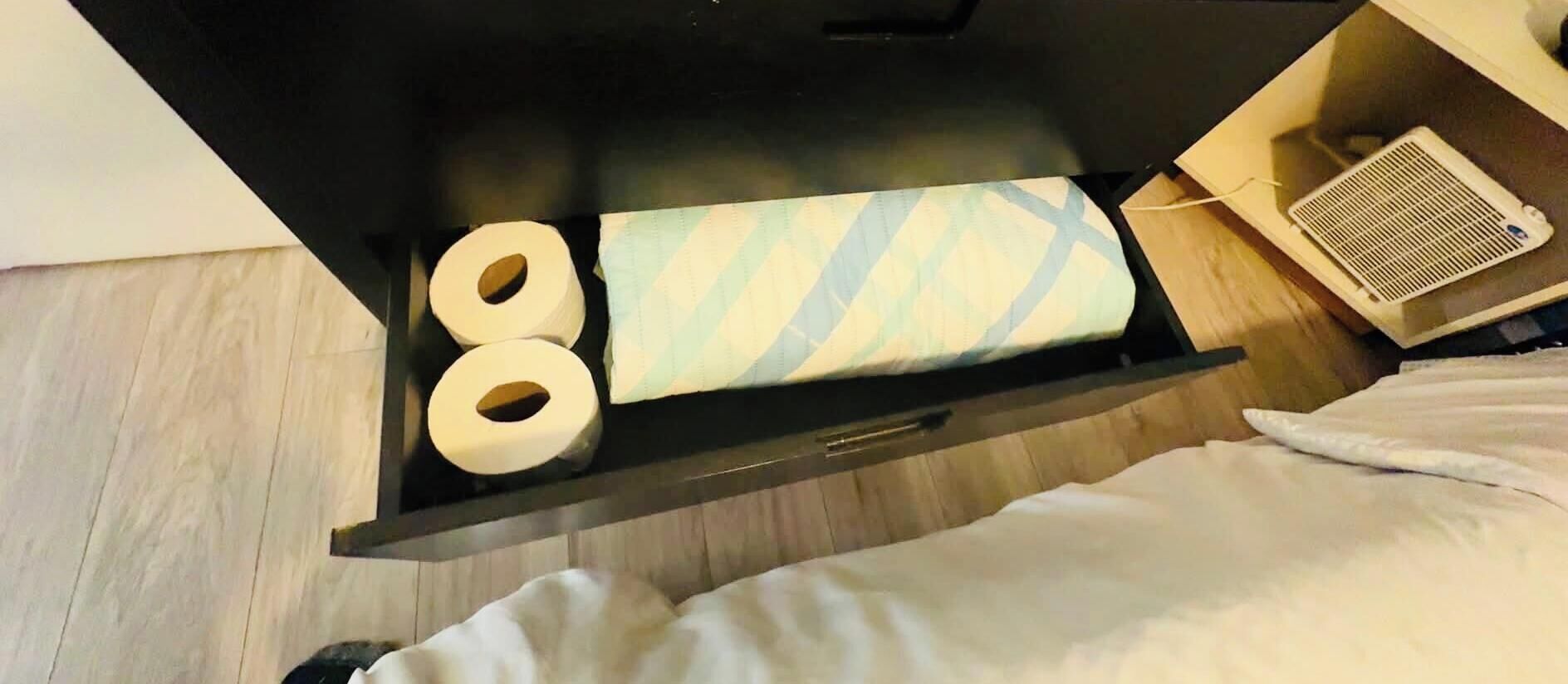 A hotel room with a bed, a bedside table with a lamp, and a window.