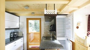 A compact kitchen with a built-in oven, a sink, and a window overlooking a wooden deck. - Chalet in Königsleiten with Wellness & Alps View (Hochkrimml)