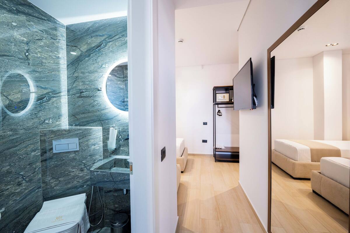 Una habitación de hotel moderna con pared de mármol, televisor de pantalla plana, un sofá y una pequeña mesa.