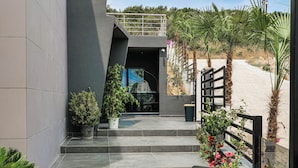 A modern outdoor seating area with tables and chairs, a staircase leading to a building entrance, and potted plants. - The Lord's Garden (Ksamil)