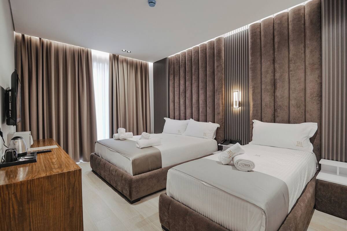 Una habitación de hotel moderna con dos camas, un escritorio de madera y televisión.