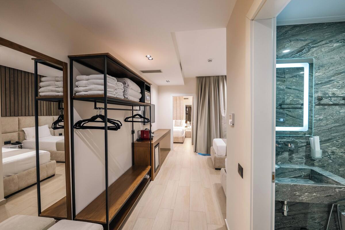 Una habitación de hotel moderna con vestidor, cama grande, baño con lavamanos de mármol y vistas a la ciudad.