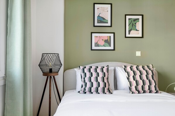 Un lit bien fait, agrémenté d’oreillers à motifs, une lampe fixée au mur et deux œuvres d’art encadrées qui décorent le mur.