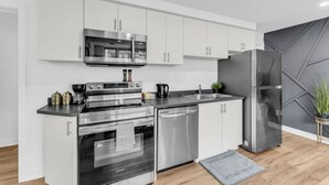 A modern kitchen with stainless steel appliances, white cabinetry, and a grey accent wall. - Your Comfort Spot in Niagara |Mins away from Falls (Niagara Falls)