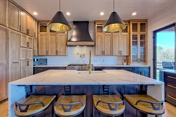 Una cocina moderna con una isla grande, armarios de madera e iluminación colgante.