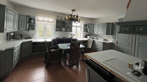 Una cocina con gabinetes grises, una mesa de comedor con sillas, una araña y una ventana con cortinas.