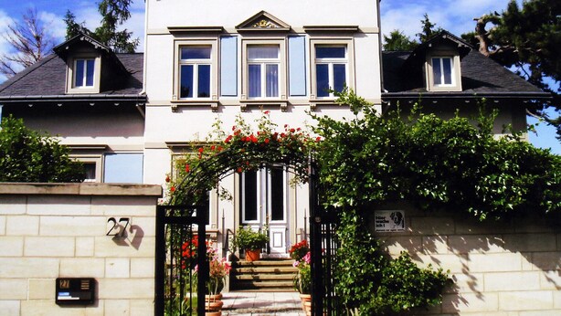Una casa de dos pisos con una entrada central, un pequeño porche y una escalera que conduce a la puerta principal.