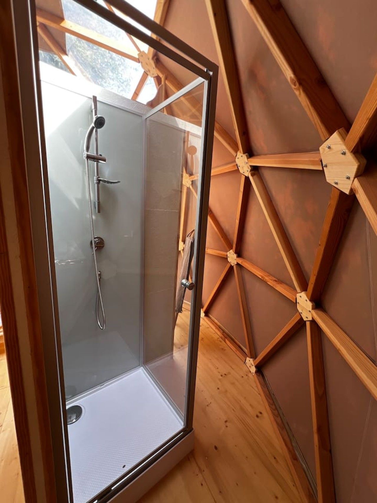 Ducha con cerramiento de vidrio, estructura de techo de madera y suelo de madera visible.
