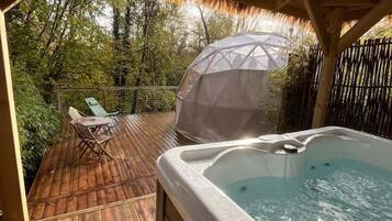 Une terrasse en bois avec un jacuzzi, des chaises longues et une structure recouverte d’un toit de chaume.