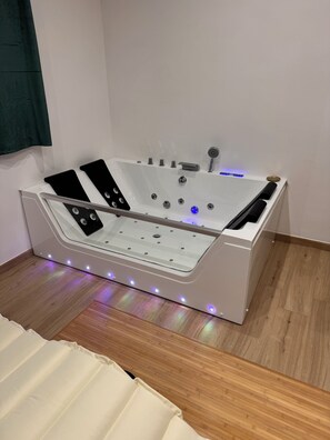 A modern, white, freestanding bathtub with built-in controls and LED lighting, placed on a wooden floor.